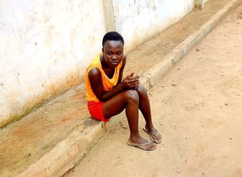 Portrait of smiling young woman sitting against wall