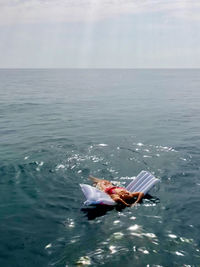 High angle view of woman lying over inflatable raft in sea against sky