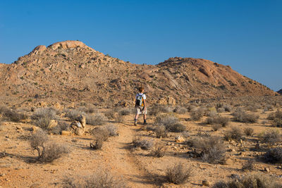 Full length of man walking on arid landscape against clear sky