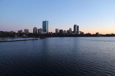 Sea by buildings against clear sky during sunset