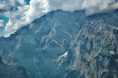 Scenic view of rocky mountains against cloudy sky on sunny day