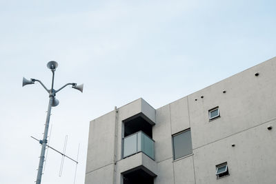 Low angle view of megaphones on pole by building against sky