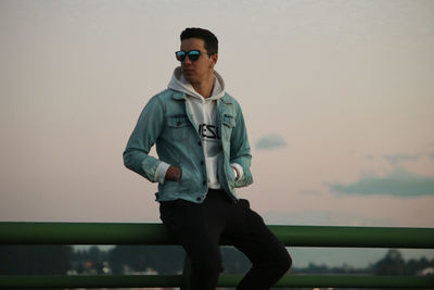 Young man wearing sunglasses standing against sky