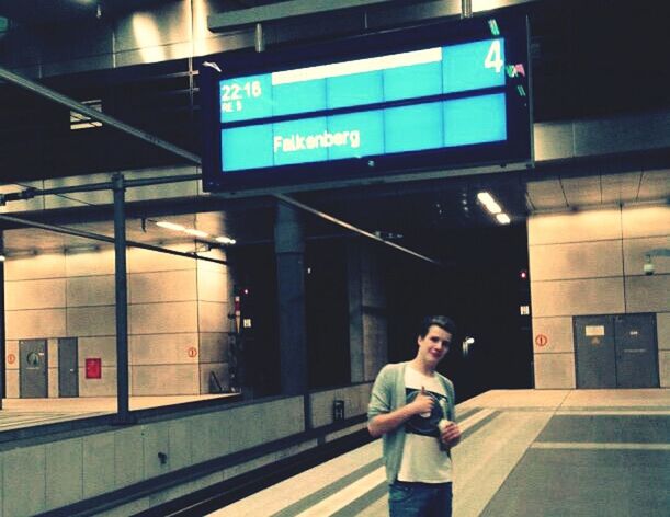 indoors, communication, lifestyles, text, casual clothing, built structure, leisure activity, standing, architecture, western script, young men, railroad station, young adult, public transportation, illuminated, railroad station platform, three quarter length, technology