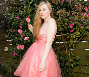 Beautiful young woman standing by pink flowering plants