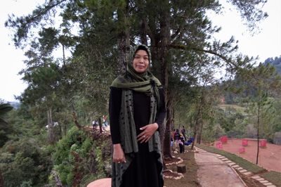 Portrait of woman standing by tree against plants