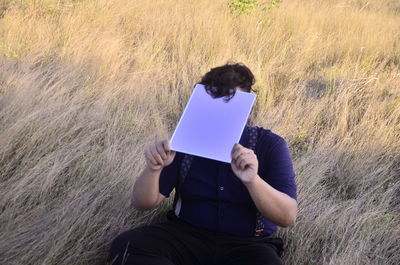 Man holding mobile phone while sitting on field