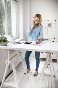 Smiling businesswoman wearing mask while talking on phone at office