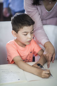 Midsection of mother assisting son in homework at home