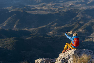 Young woman standing on rocks on top of a mountain making a selfie.