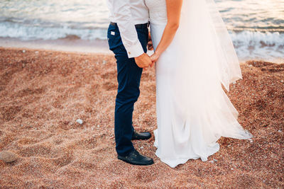 Low section of couple holding hands at beach