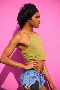 Side view of young woman standing against pink wall
