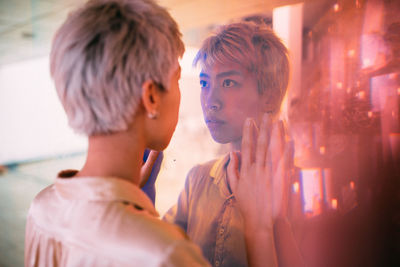 Rear view of woman standing in front of glass with reflection