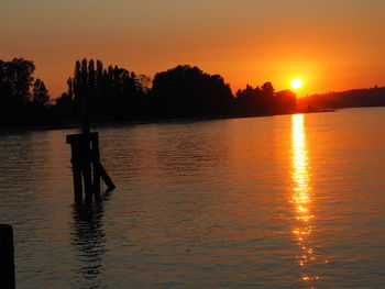 Silhouette wooden posts in lake against sky during sunset