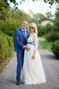 Full length portrait of happy newlywed couple standing on footpath at park