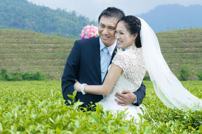 Smiling bridal couple standing amidst plants on field