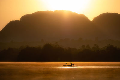 Silhouette people on boat against orange sky