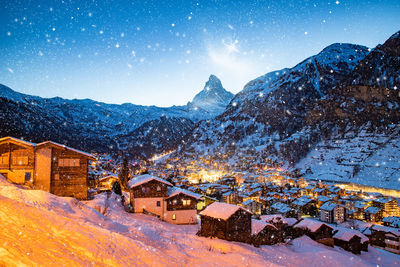 Houses by snow covered mountains against sky at night