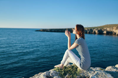 Woman sitting on rock looking at sea against sky