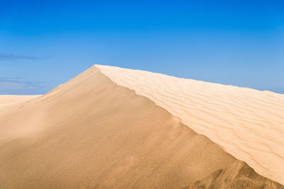 Low angle view of sand dunes against blue sky