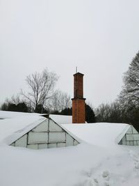 Snow covered field by building against sky