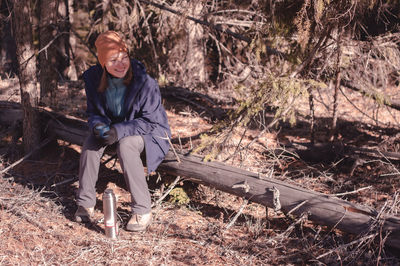 A person with thermos in morning forest sitting on a log and looking at sunlight