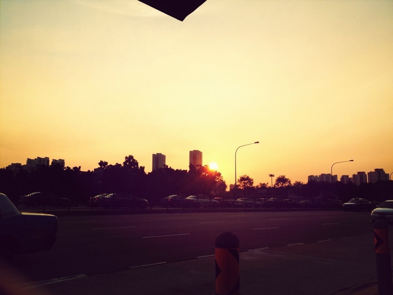 sunset, city, building exterior, architecture, car, built structure, transportation, street, clear sky, road, land vehicle, silhouette, city life, mode of transport, sky, lifestyles, men, skyscraper