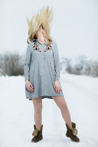 Full length of woman tossing hair while standing on snow covered land