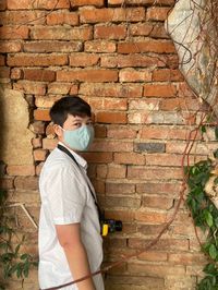 Portrait of woman wearing mask standing against brick wall