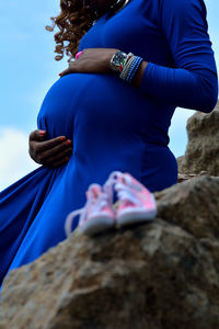 Baby booties on rock against pregnant woman with hands on stomach