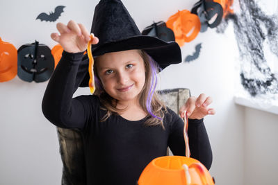 Little girl in costume of witch holding pumpkin jack with candies, celebrating halloween at home