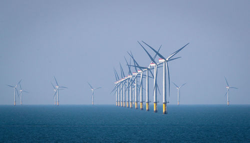 Wind turbines in sea against clear sky