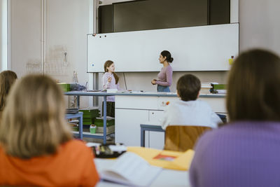 Teacher standing and talking with female student near whiteboard in classroom