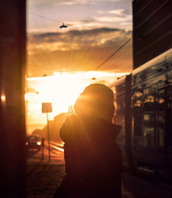 Silhouette woman standing in city against sky during sunset