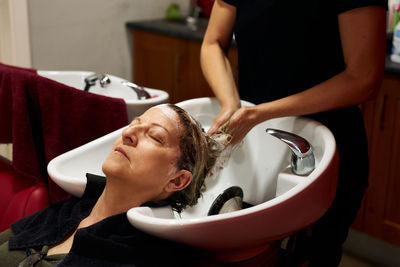 Hairdresser washes her client's hair in her salon