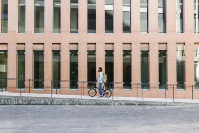 Man wheeling with bicycle by building