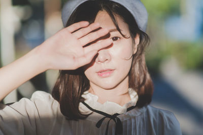 Close-up portrait of young woman shielding eyes on sunny day