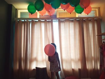 Girl holding balloon against window