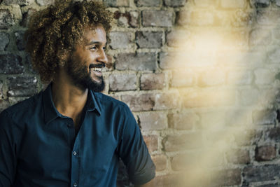 Smiling man with beard and curly hair at brick wall