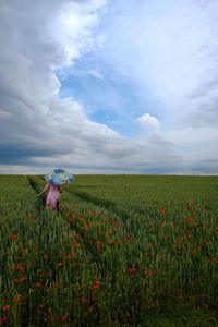 Rear view of woman with umbrella amidst poppies on landscape against sky