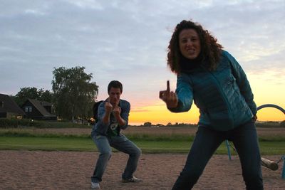 Portrait of friends showing middle finger at playground against sky during sunset