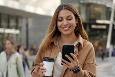 Business woman walks watching mobile phone with blurred people on modern urban background