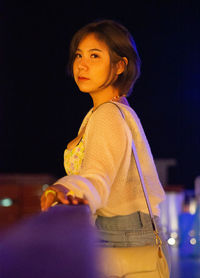 Portrait of young woman standing against sky at night