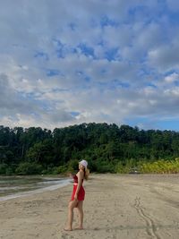 Rear view of woman standing at beach against sky