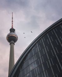 Low angle view of fernsehturm against cloudy sky