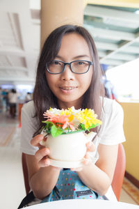 Portrait of smiling young woman holding artificial flowers in restaurant