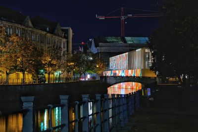 Illuminated buildings by street against sky at night