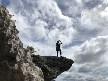 Low angle view of man standing on rock against sky