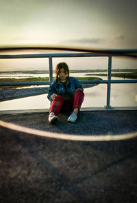 Woman sitting against railing during sunset