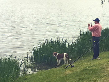 Rear view of man with dog standing by lake